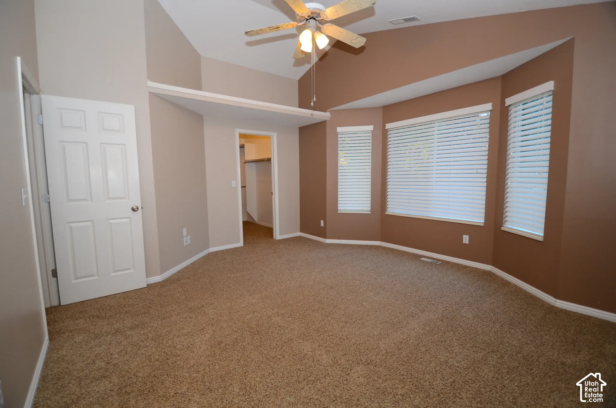 Vaulted ceiling with a ceiling fan, bay window configuration with white blinds, carpeted flooring, and a walk-in closet