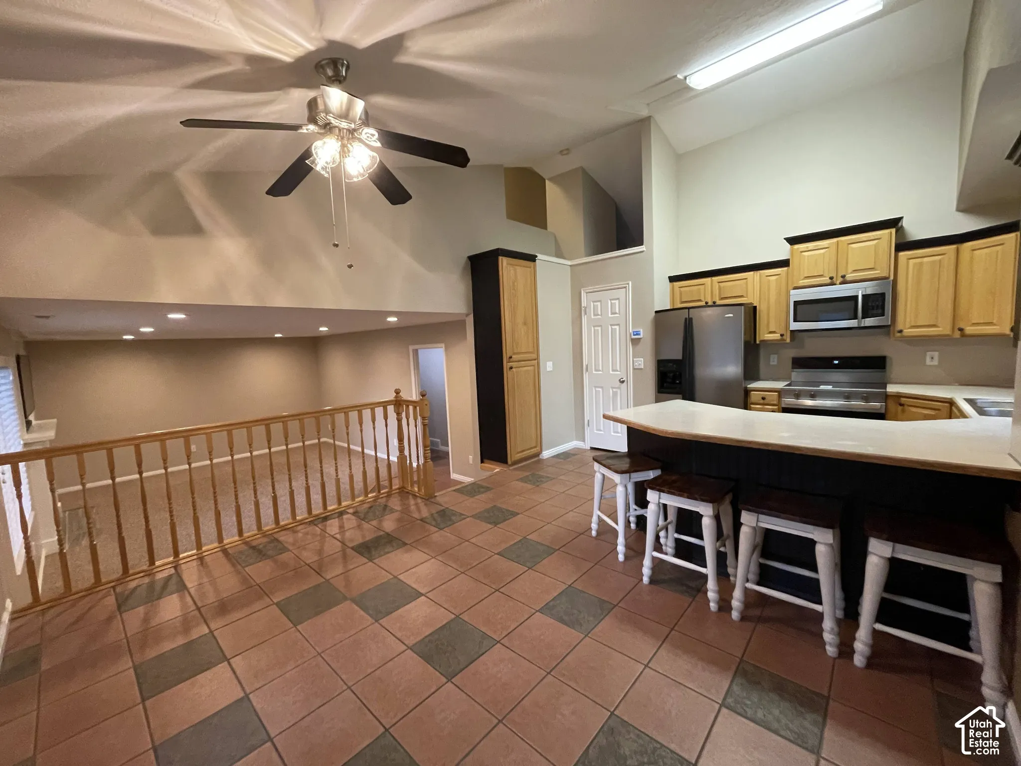 Vaulted ceilings, kitchen with wood-finish cabinetry, stainless steel appliances, breakfast bar, and tile flooring