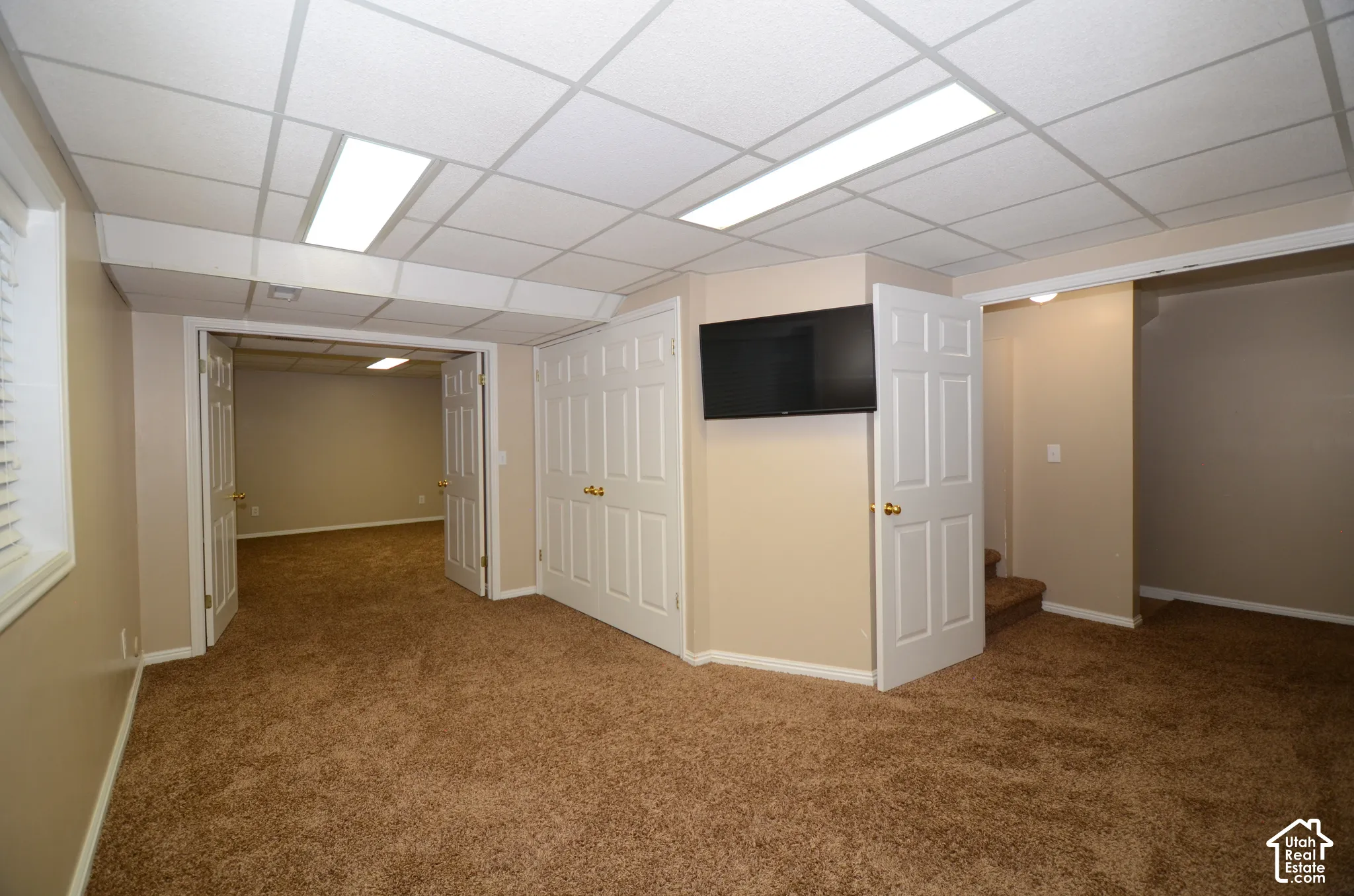 Carpeted room featuring a drop ceiling with recessed lighting, double bifold closet doors, and French doors opening to an additional room