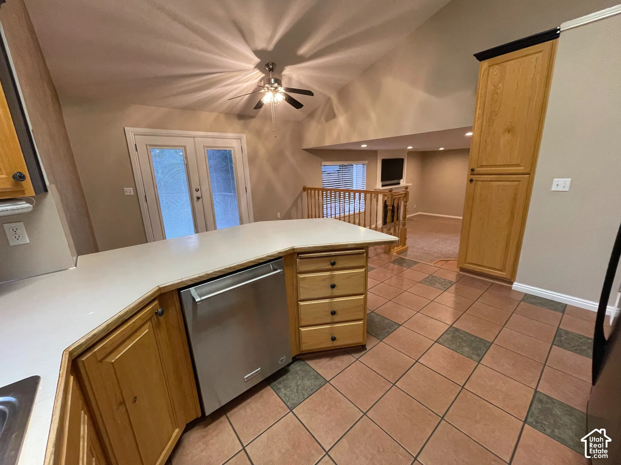 Kitchen island with solid surface countertop, stainless steel dishwasher, wood-finish cabinetry, and tiled flooring