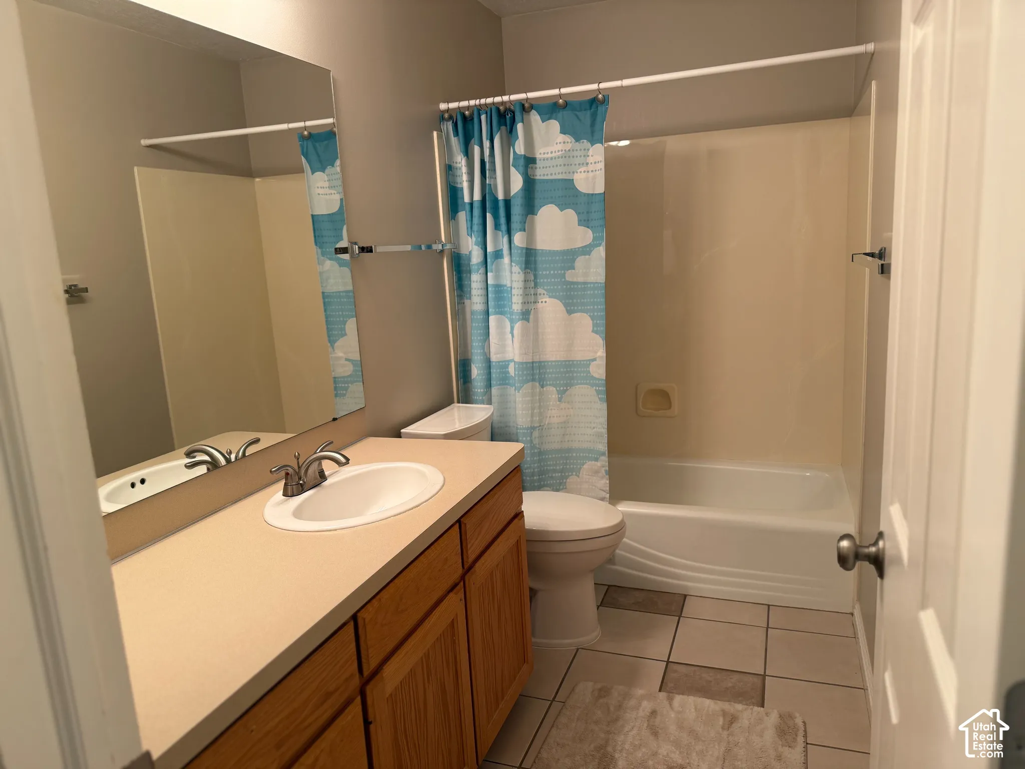 Bathroom featuring a built-in vanity with a single basin sink, a large wall-mounted mirror, a toilet, a full bathtub with shower surround, and tiled flooring