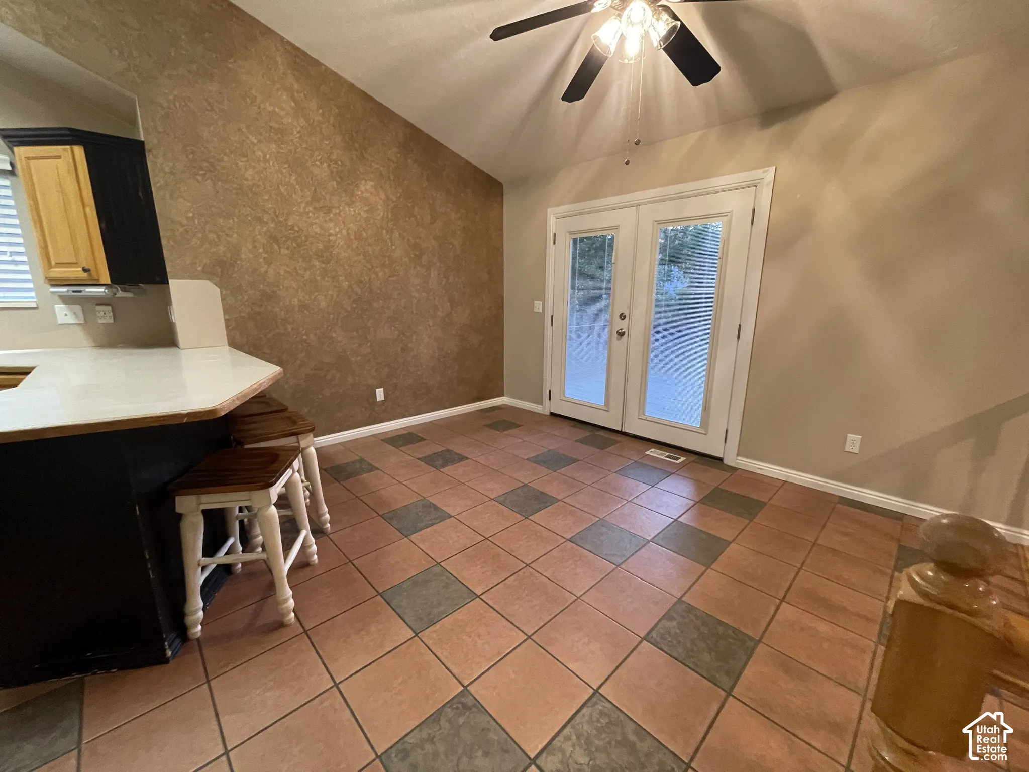Vaulted ceiling with a ceiling fan, French doors, tiled flooring with a checkerboard pattern, breakfast bar, and wood-finish cabinetry
