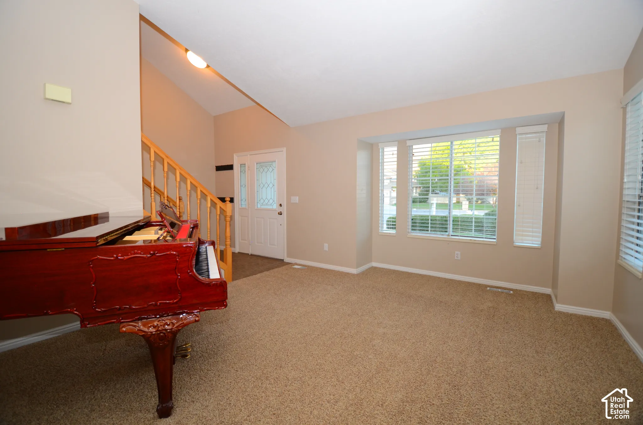 Spacious room featuring vaulted ceilings, bay windows with blinds, and neutral carpeting
