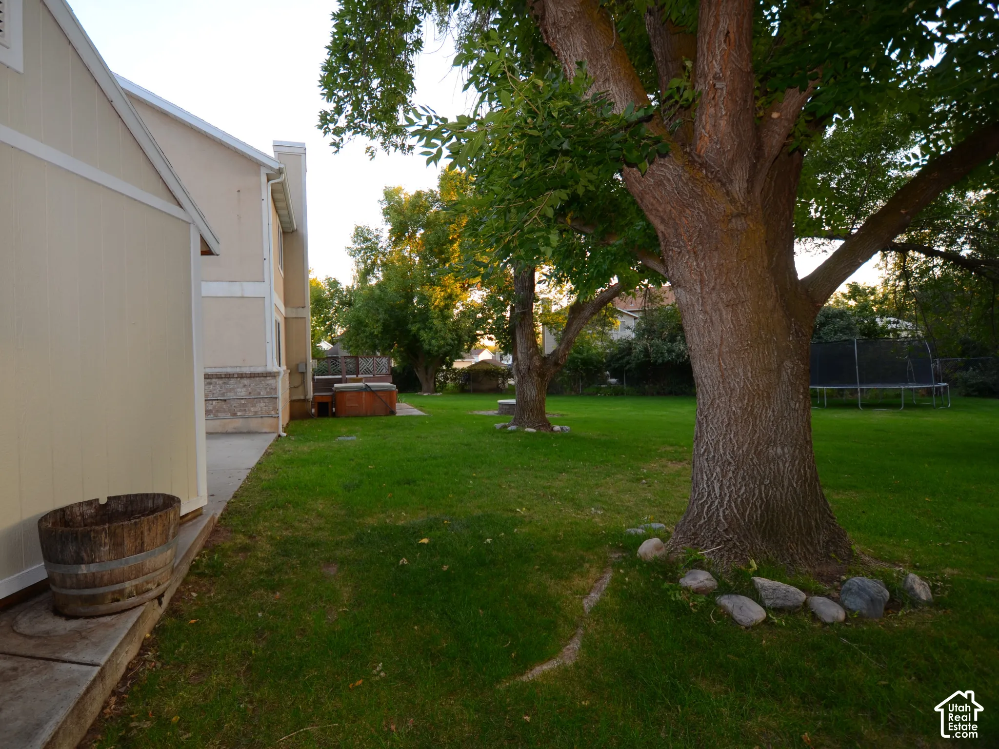 Expansive grassy yard with mature trees and a concrete pathway leading to a built-in spa