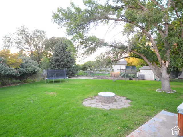 Expansive backyard oasis featuring a manicured lawn, mature shade trees, and a stone-lined fire pit