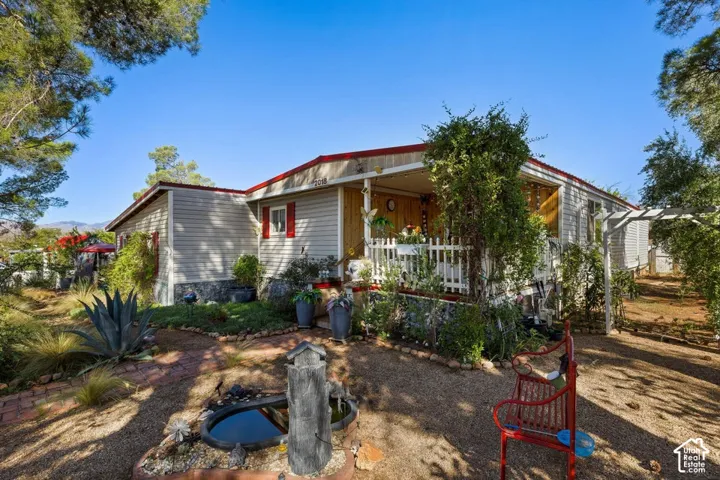 Front exterior featuring horizontal siding, red trim accents, a covered porch with white picket railing, and landscaped grounds with a water feature