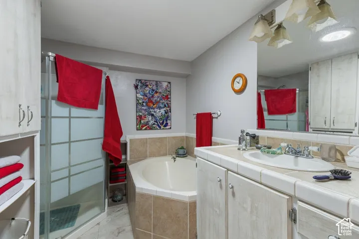 Tile-surround corner soaking tub, glass-enclosed shower, dual-sink vanity with tile countertop, and built-in cabinetry