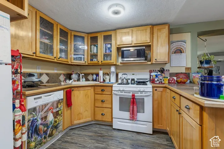 Wood-finish flooring, wood cabinetry with glass-front upper cabinets, built-in microwave, gas range, and stone tile backsplash