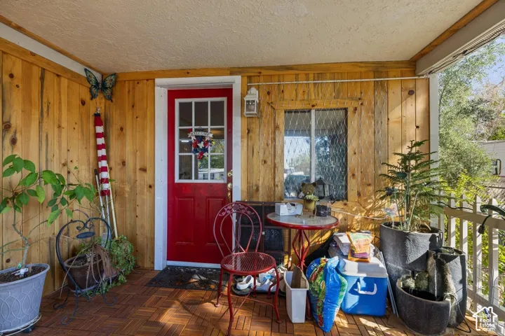 Covered porch featuring wood-finish paneling, a red entry door with glass inserts, a single window with textured glass, and a wood-finish tile floor