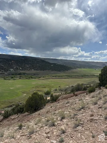 Expansive elevated landscape featuring varied terrain, distant green fields, and surrounding natural hills