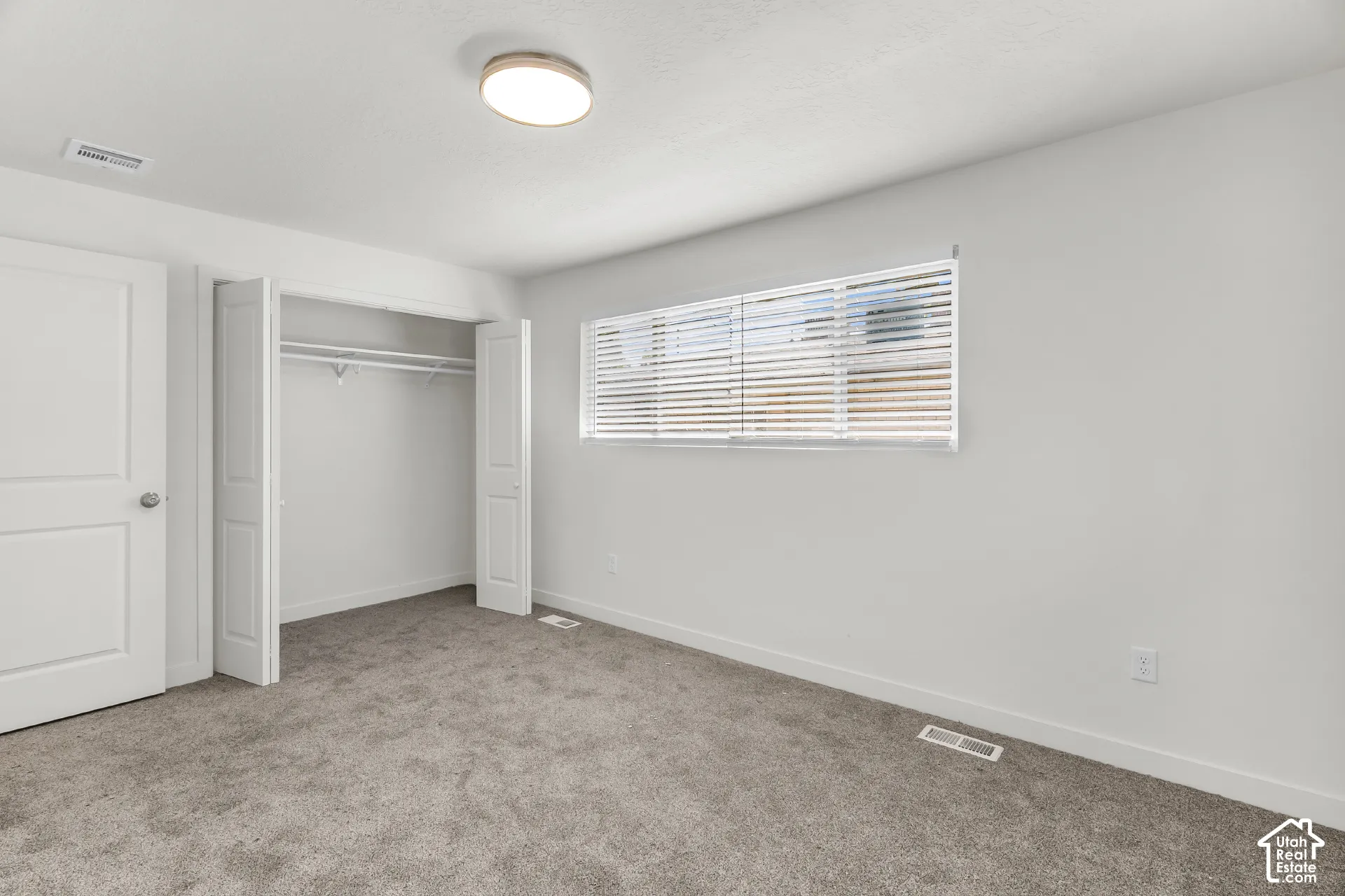 Neutral wall paint, gray carpeting, bi-fold closet doors, and a window with horizontal blinds