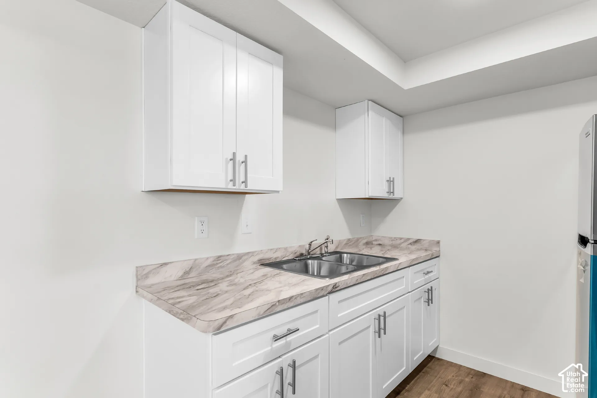 White shaker cabinetry with brushed nickel hardware, laminate countertops, dual-basin stainless steel sink, and wood-finish flooring