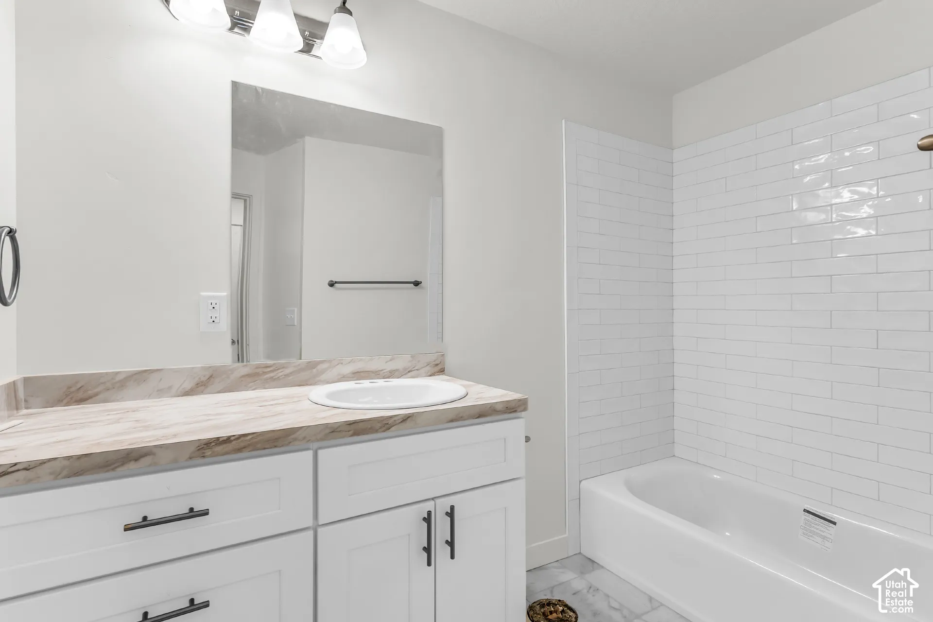 White shaker-style vanity with dark hardware, integrated sink, and patterned countertop