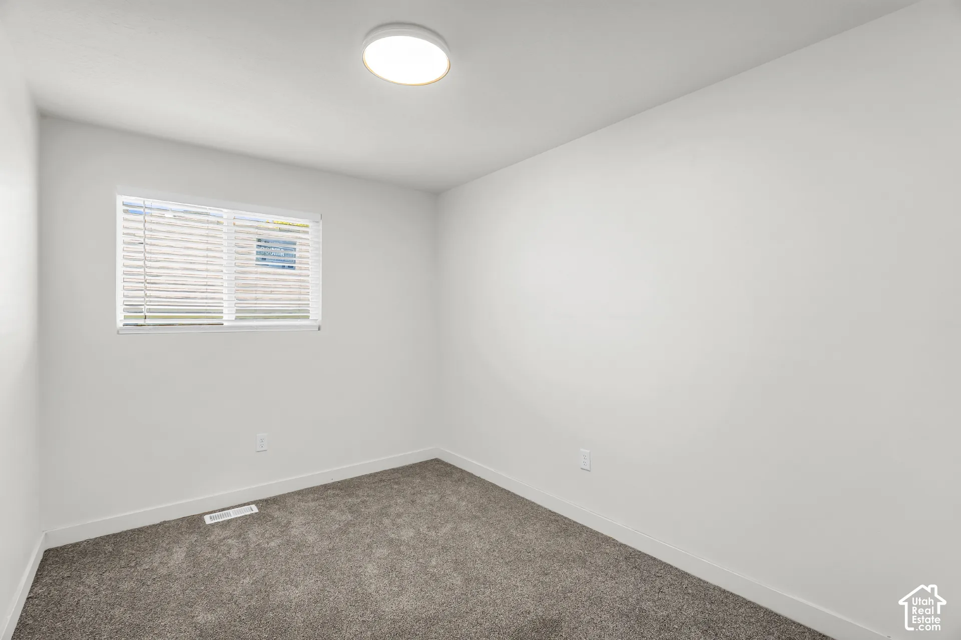 Window with blinds, wall-to-wall carpeting, white walls, and a flush mount ceiling light