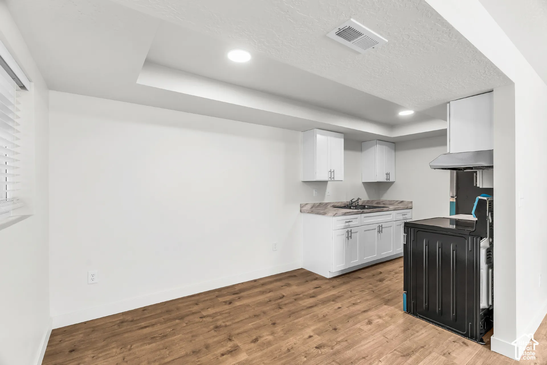 Recessed lighting, wood-finish flooring, white cabinetry with silver hardware, dark sink, and stainless steel range hood