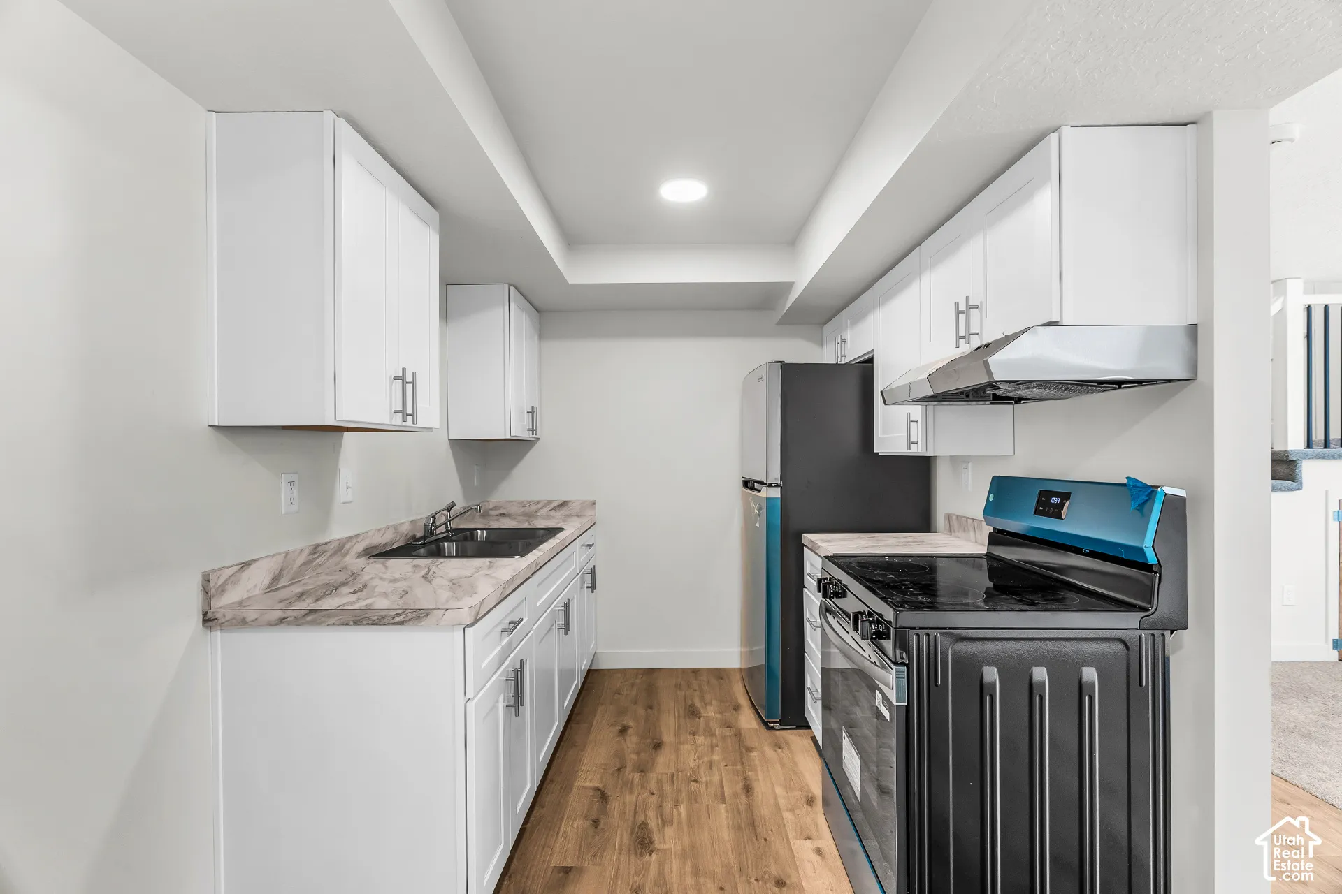 White cabinetry, wood-finish flooring, undermount sink, black appliances, and recessed lighting