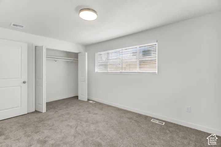 Neutral wall paint, gray carpeting, bi-fold closet doors, and a window with horizontal blinds