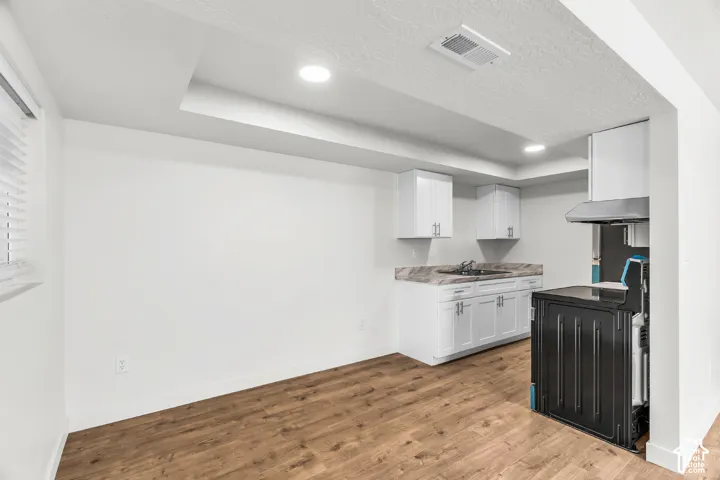Recessed lighting, wood-finish flooring, white cabinetry with silver hardware, dark sink, and stainless steel range hood