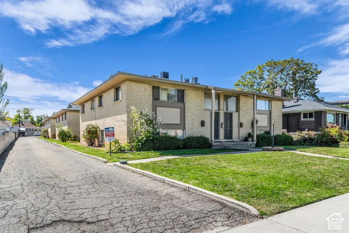 Brick exterior with large windows, mature landscaping, and a paved driveway