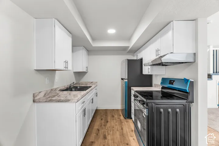 White cabinetry, wood-finish flooring, undermount sink, black appliances, and recessed lighting