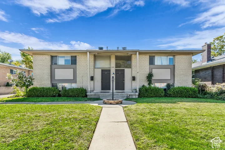 Brick exterior with gray accent panels, dual entry doors, concrete walkway, and landscaped front yard with green lawn