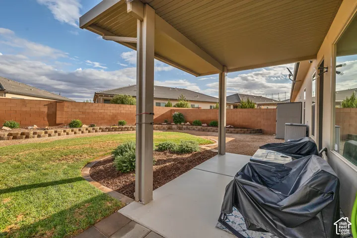 Covered patio with concrete flooring, supported by square columns, overlooking a manicured lawn