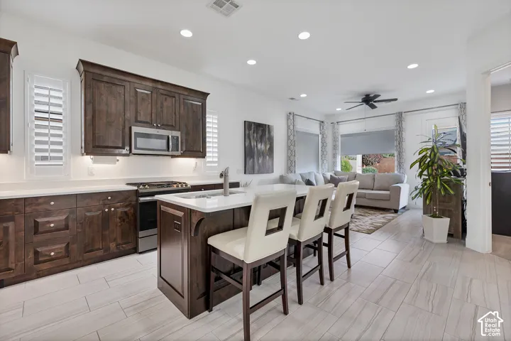 Kitchen featuring dark wood cabinetry, stainless steel appliances, white countertops, and a center island with integrated sink
