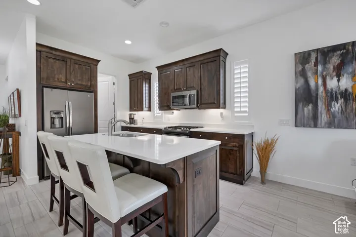 Kitchen featuring dark wood-finish cabinetry, stainless steel appliances, a center island with a light-colored countertop, recessed lighting, and light-toned tile flooring