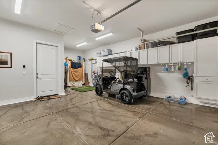 Garage featuring epoxy flooring, overhead track lighting, built-in white cabinetry, wall-mounted storage, and an interior access door