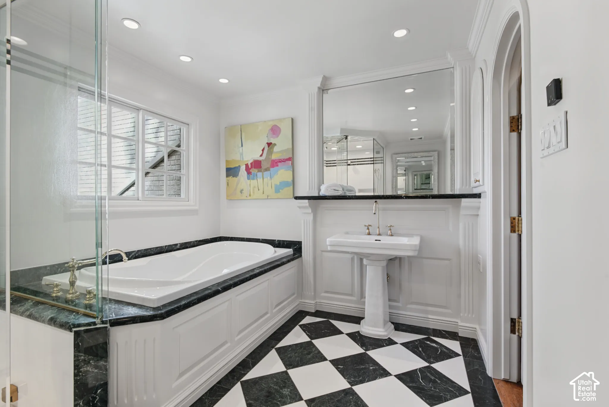 Checkered floor tile, recessed lighting, built-in soaking tub with dark stone surround, glass shower enclosure, and pedestal sink