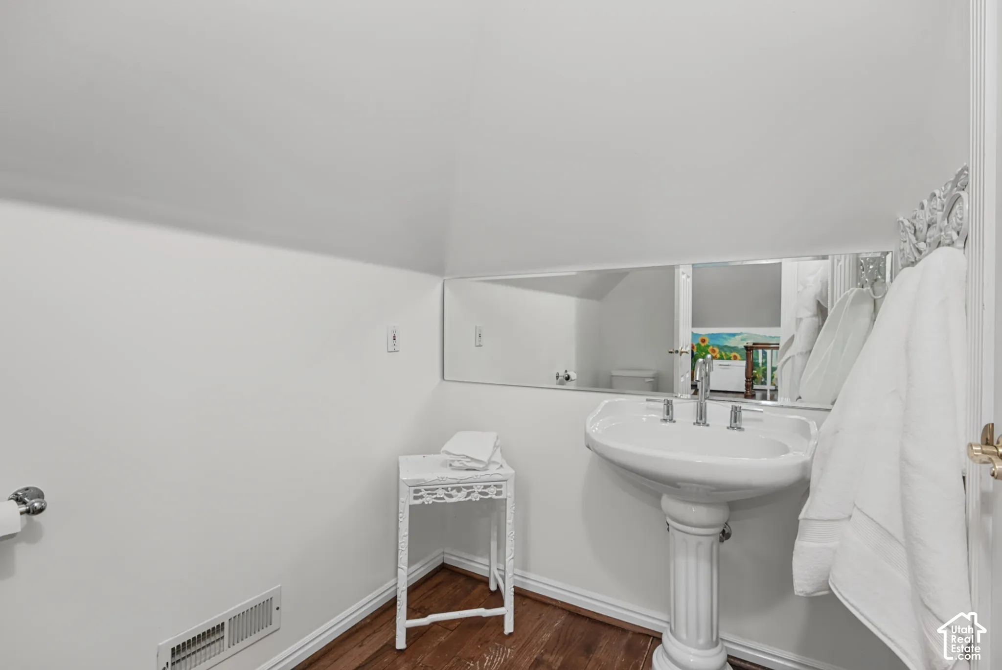 Pedestal sink, wall-mounted mirror, wood-finish flooring, white trim, and white walls