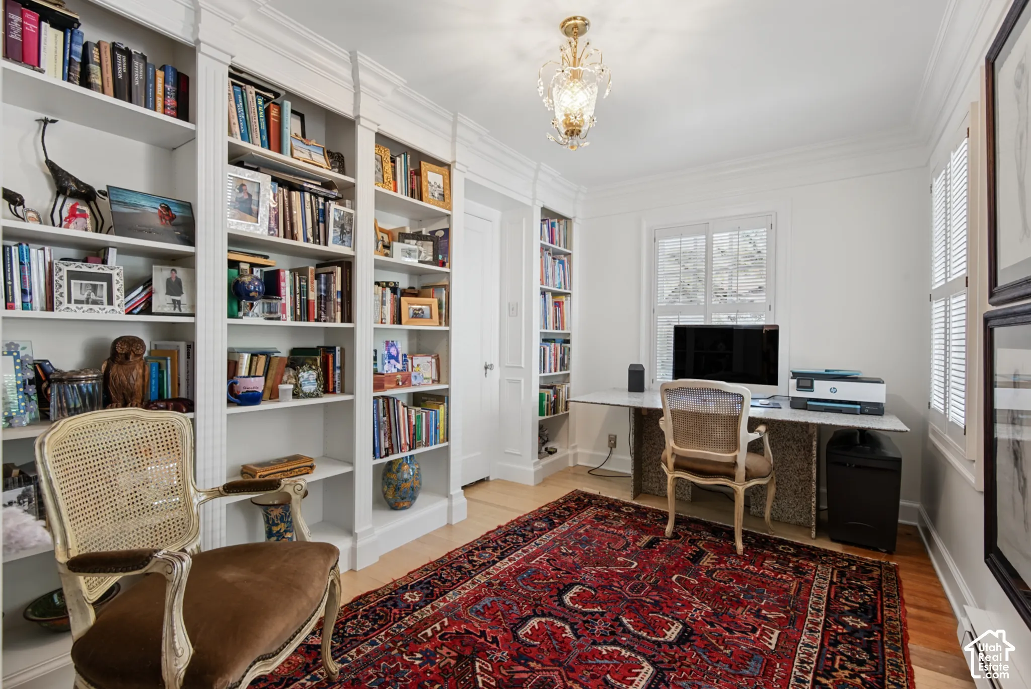 Built-in white shelving, wood-finish flooring, white plantation shutters, and an ornate ceiling fixture