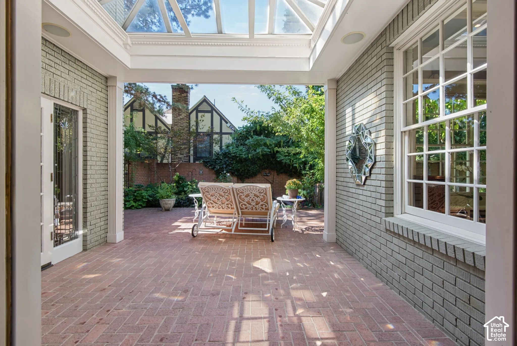 Sunlit patio featuring a brick floor, white framed double-pane window, and a glass-paneled ceiling