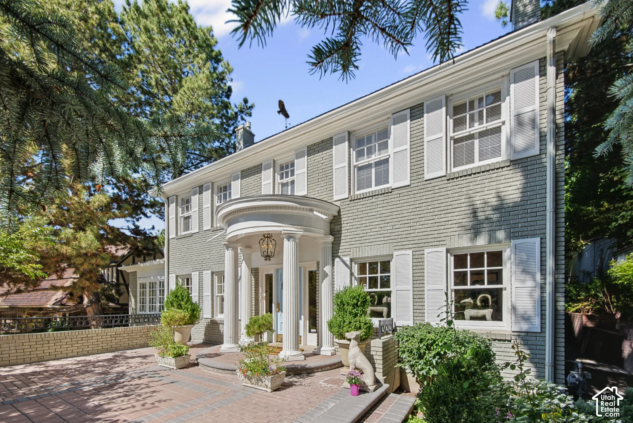 Brick exterior with white shutters, a circular portico entry with columns, a prominent front door, and a brick paver driveway