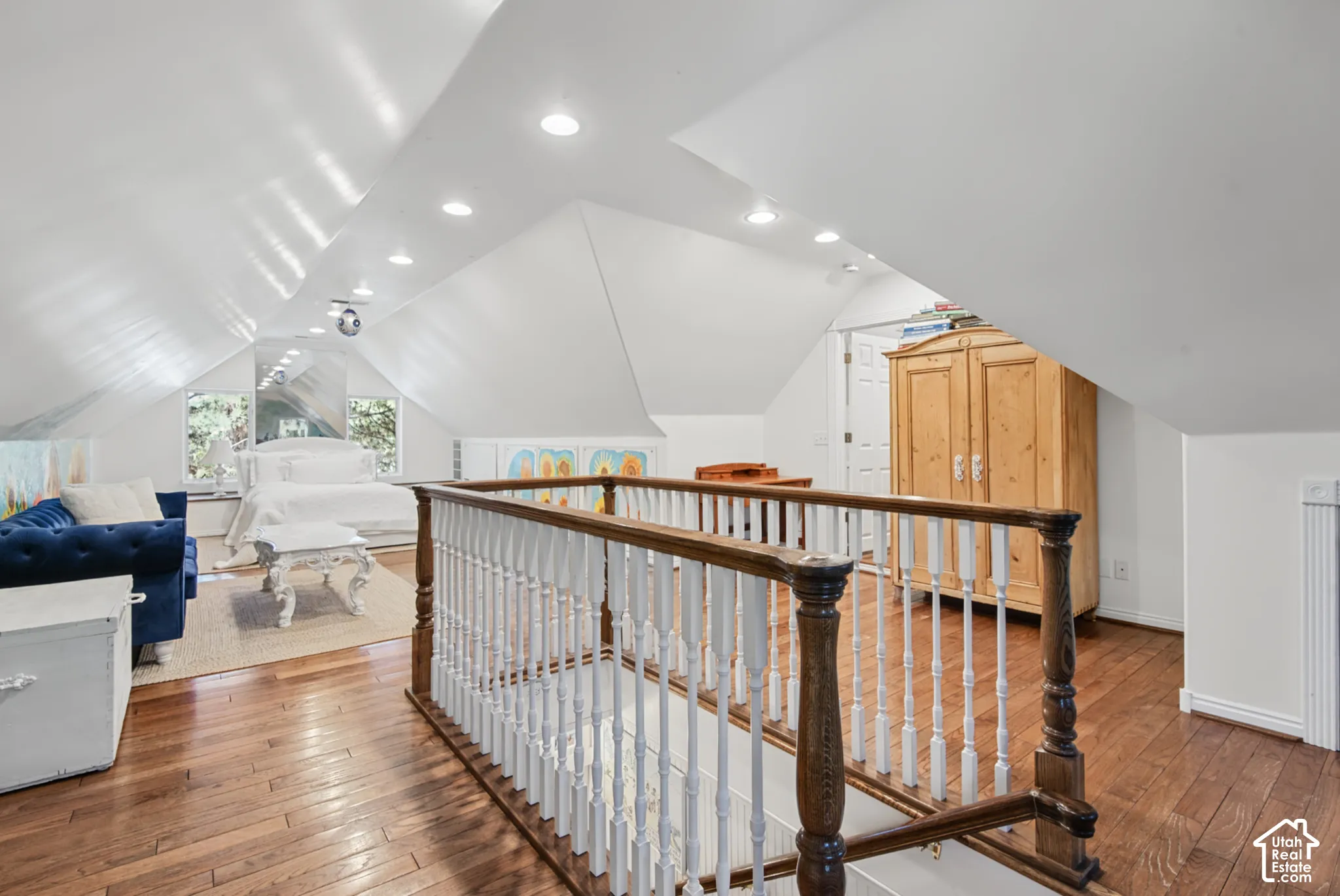 Hardwood flooring, white painted walls, recessed lighting, white wood spindle railing, and a vaulted ceiling