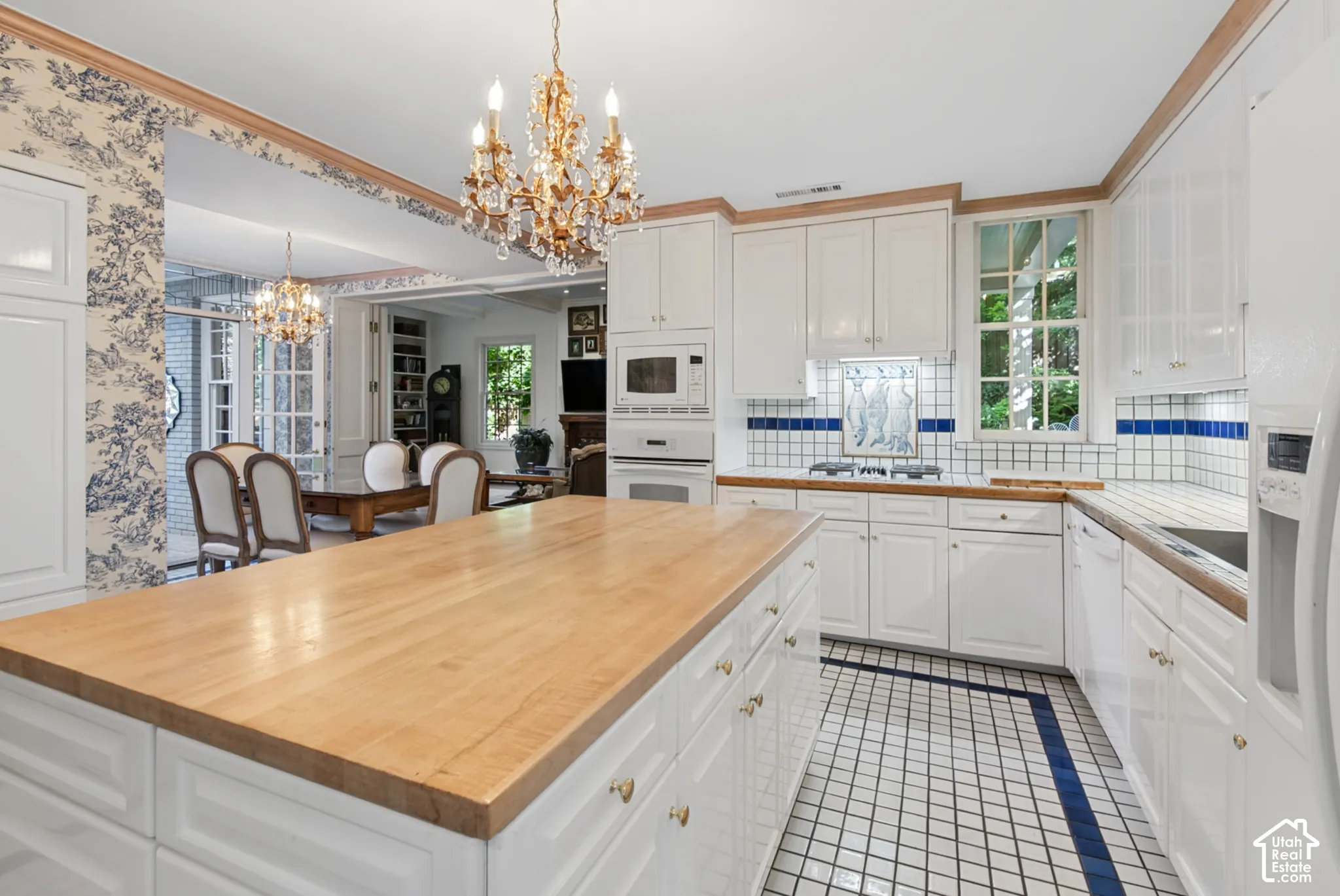 Kitchen featuring a butcher block island and countertops, white cabinetry, integrated appliances, and a tiled floor with blue accents