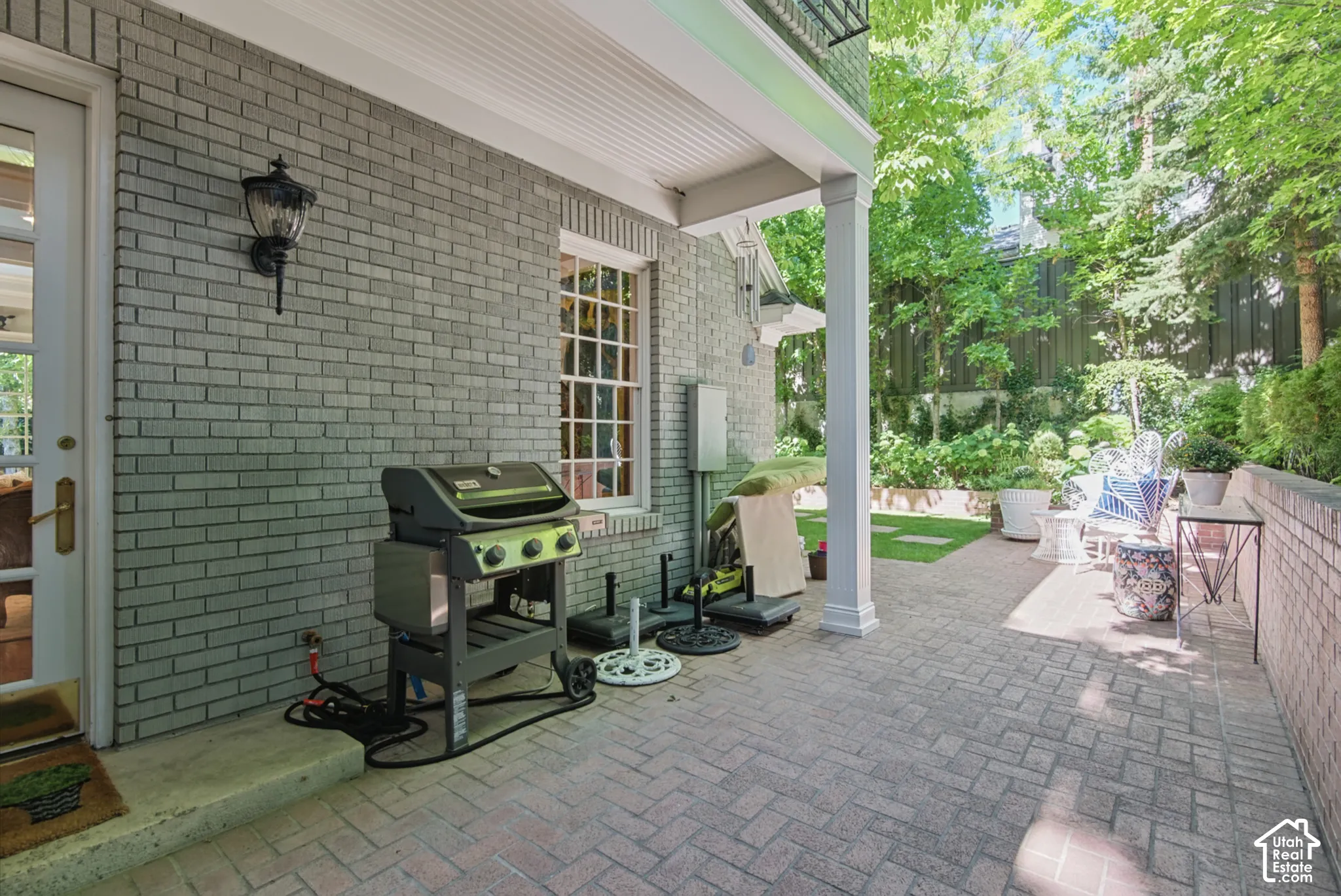 Brick exterior with a covered patio, paved hardscaping, and verdant landscaping