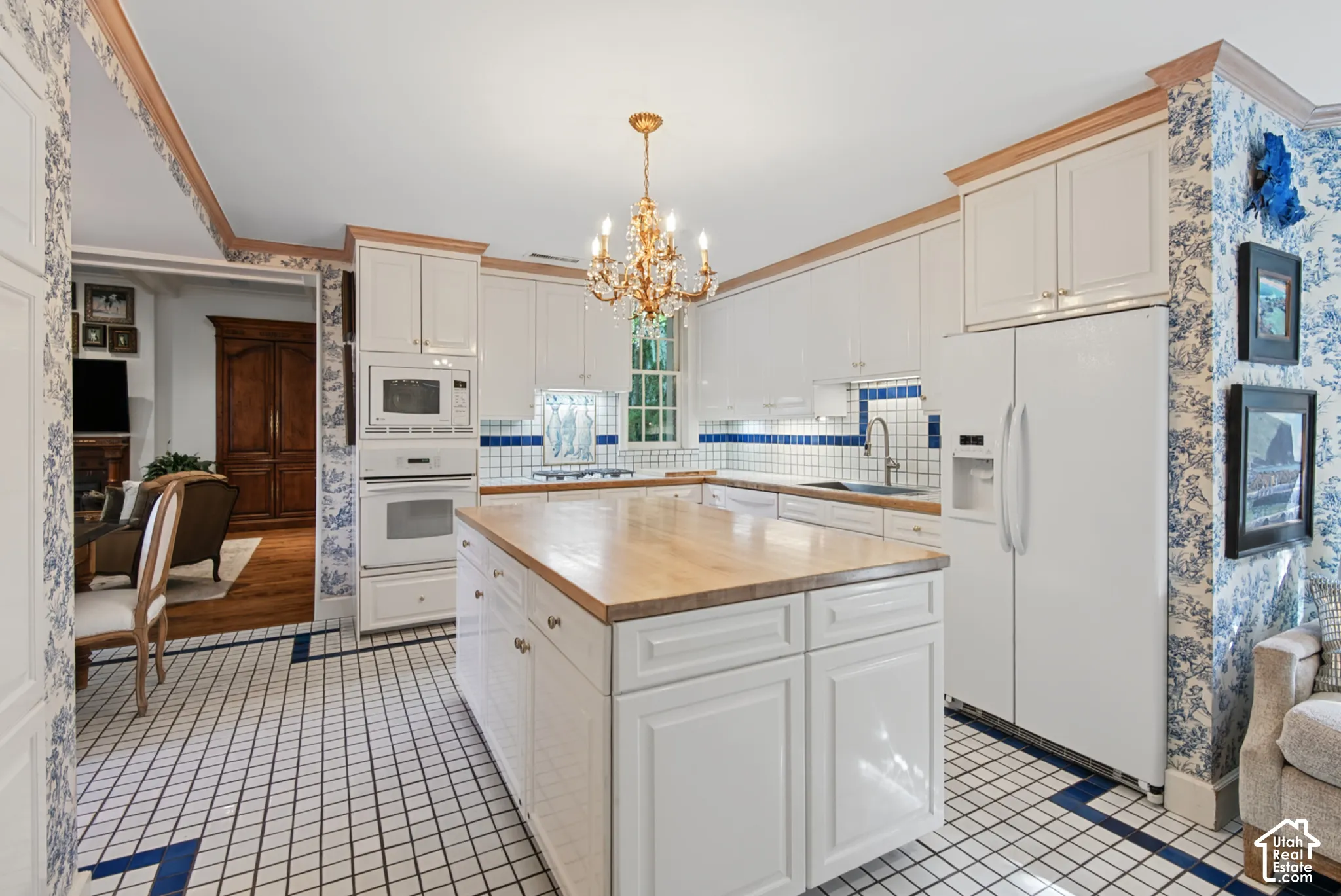 Kitchen featuring a central island with a wood countertop, white cabinetry with crown molding, integrated white appliances, and a tiled floor