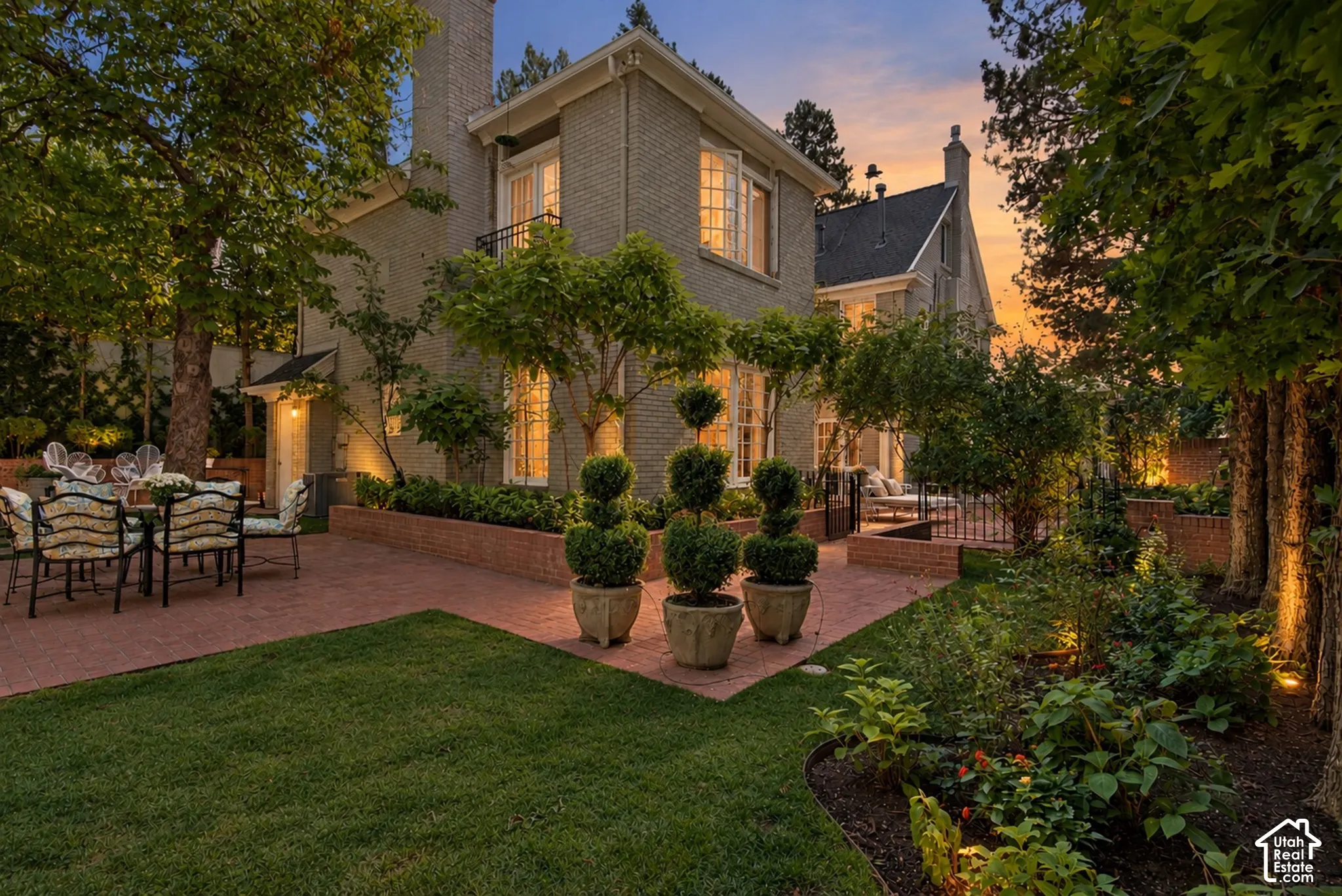 Brick exterior, paved patio, manicured lawn, established garden beds, and mature trees