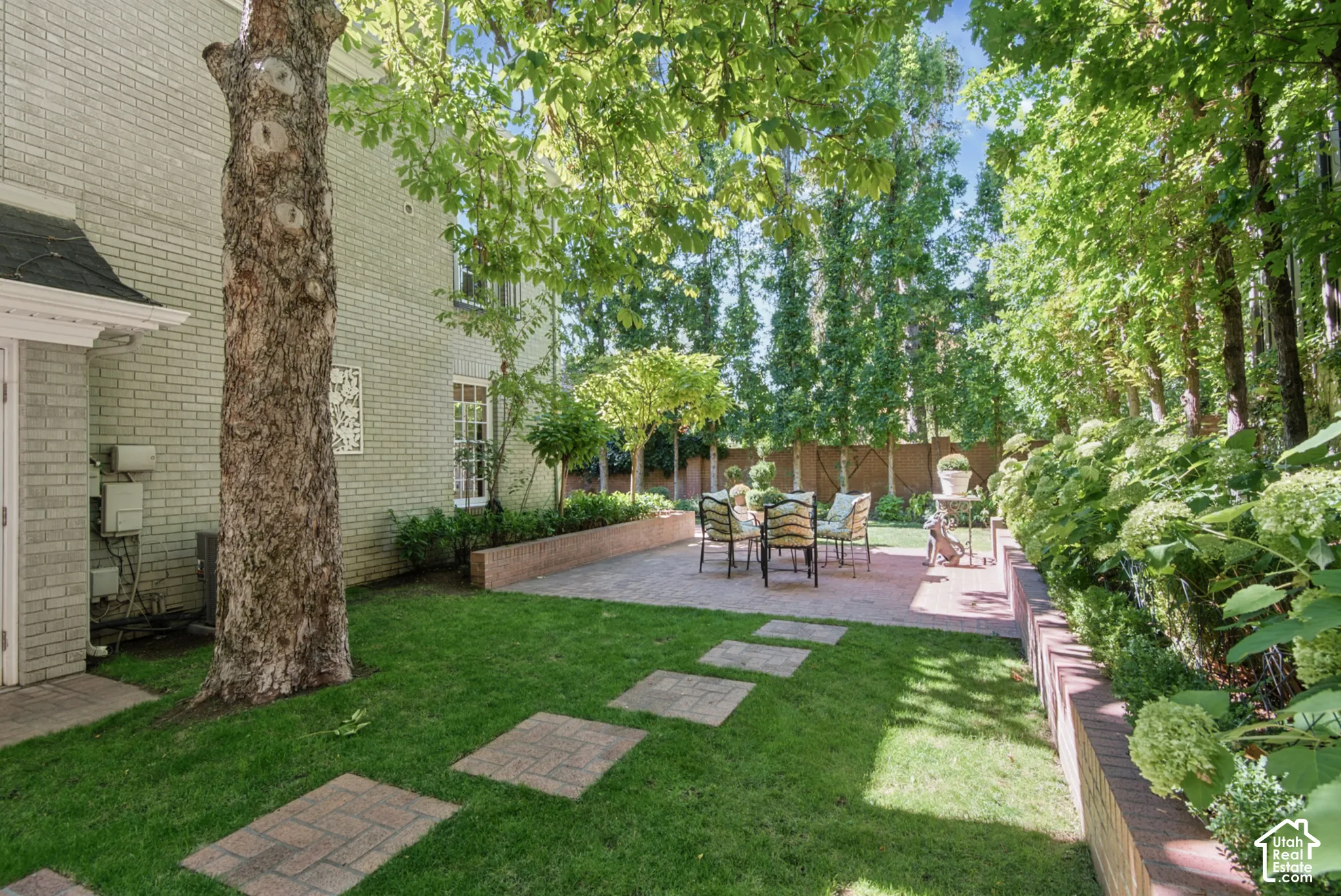 Manicured lawn with paver stepping stones, brick-edged planting beds, and a paver patio