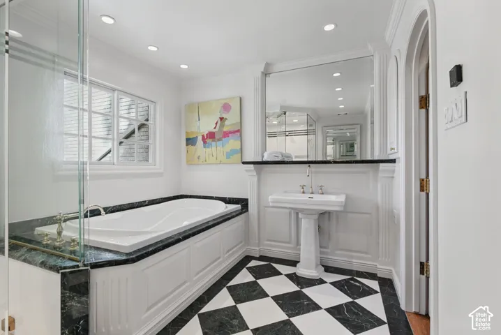 Checkered floor tile, recessed lighting, built-in soaking tub with dark stone surround, glass shower enclosure, and pedestal sink
