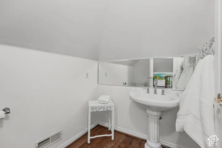 Pedestal sink, wall-mounted mirror, wood-finish flooring, white trim, and white walls
