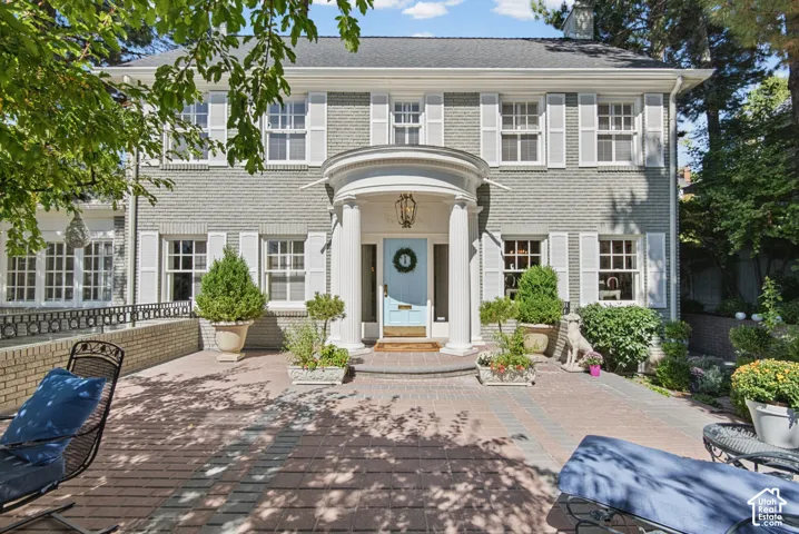 Brick exterior with white shutters, a covered entry with columns, and a paved courtyard