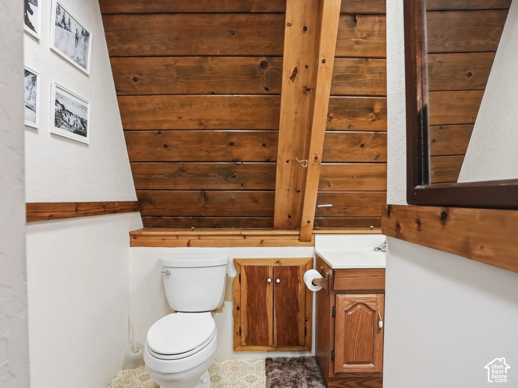 Sloped wood-plank ceiling featuring an exposed timber beam, custom wood-paneled cabinetry, and a vanity with a white countertop