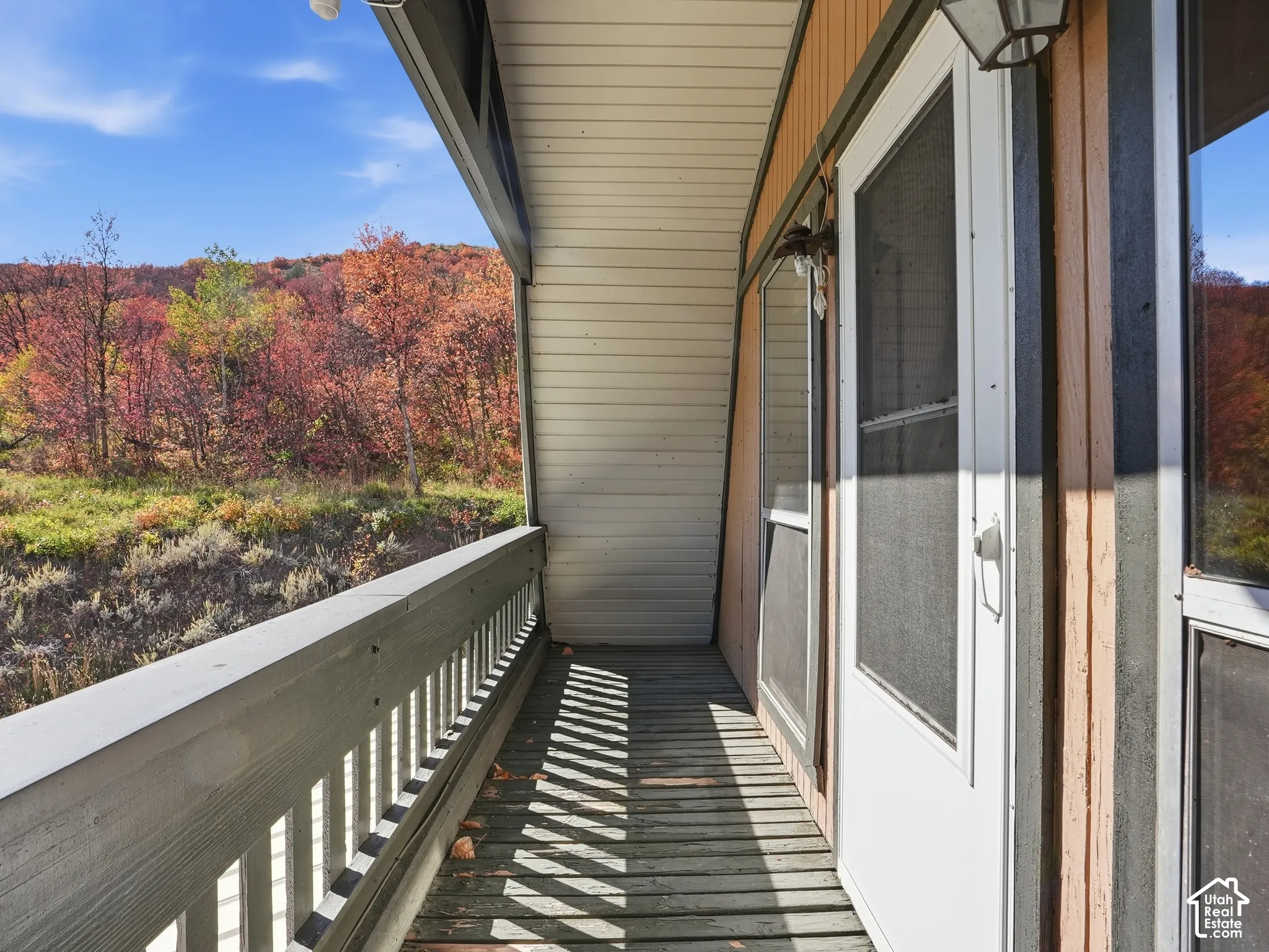 Covered exterior deck featuring wood-plank flooring, slatted railing, and white-framed entry door