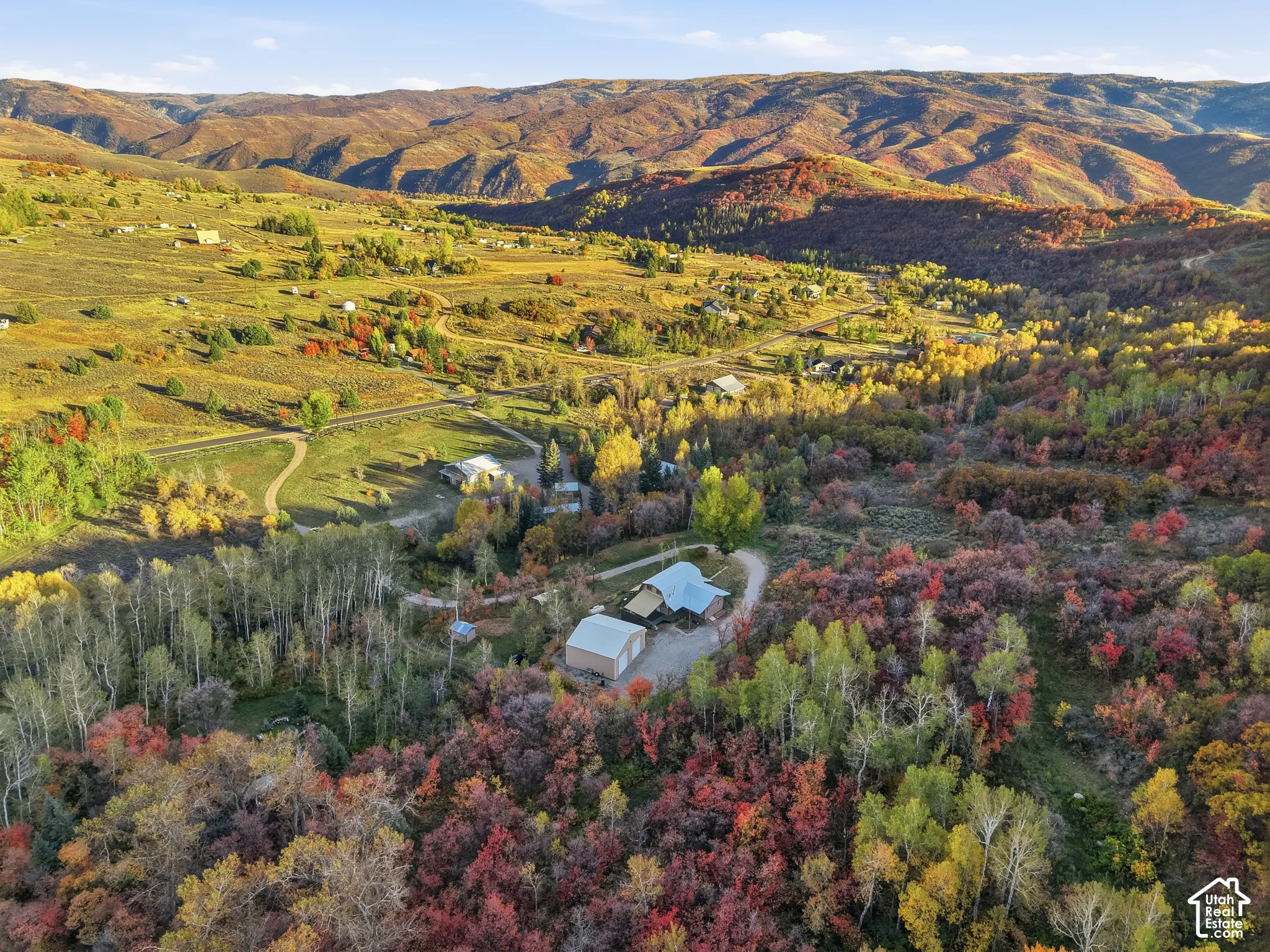 Aerial perspective of expansive acreage featuring mature deciduous forest, winding gravel paths, and mountainous terrain
