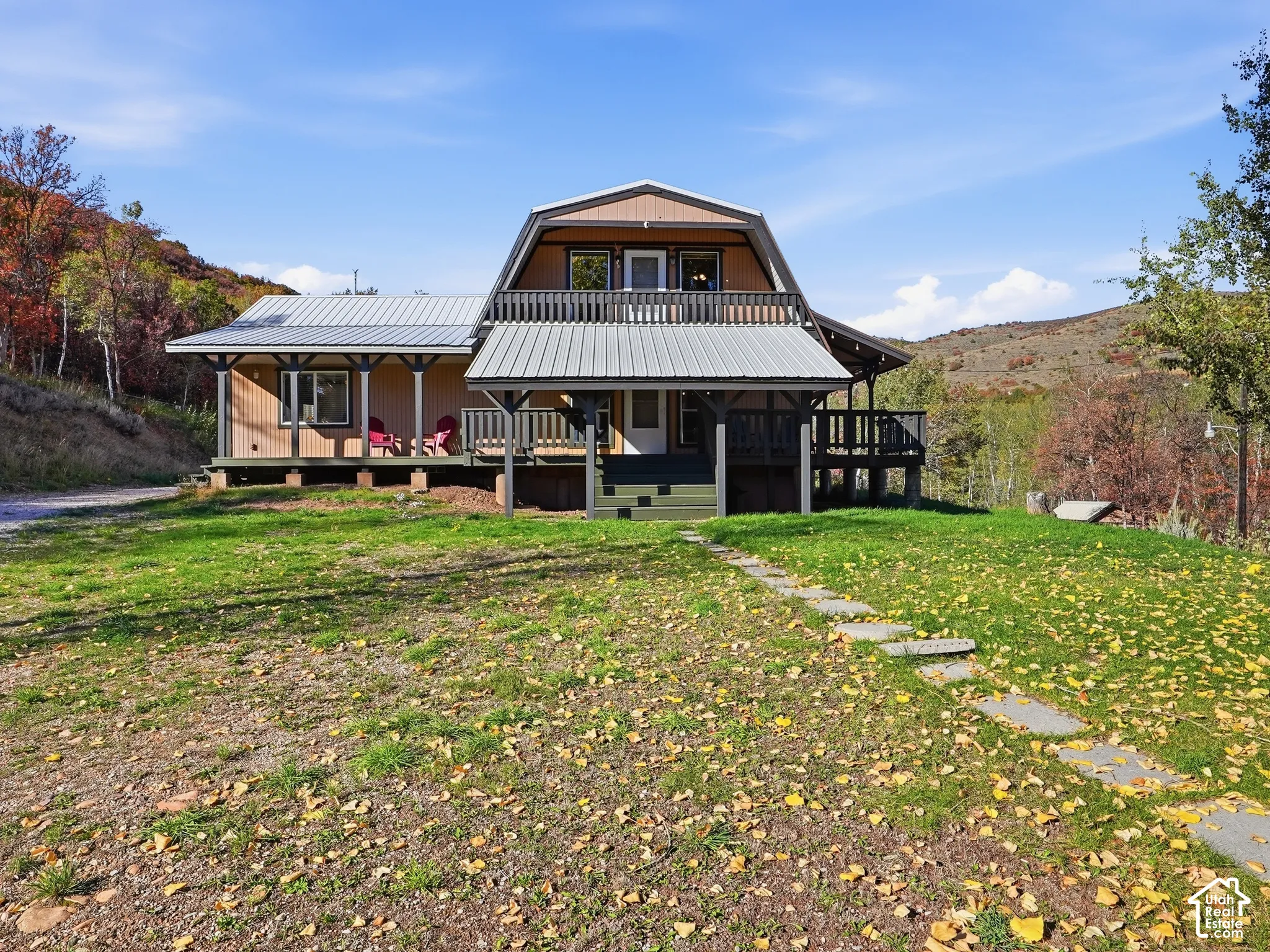 Gambrel-style exterior featuring a metal roof, tiered wrap-around deck, upper-level balcony, and stone paver walkway