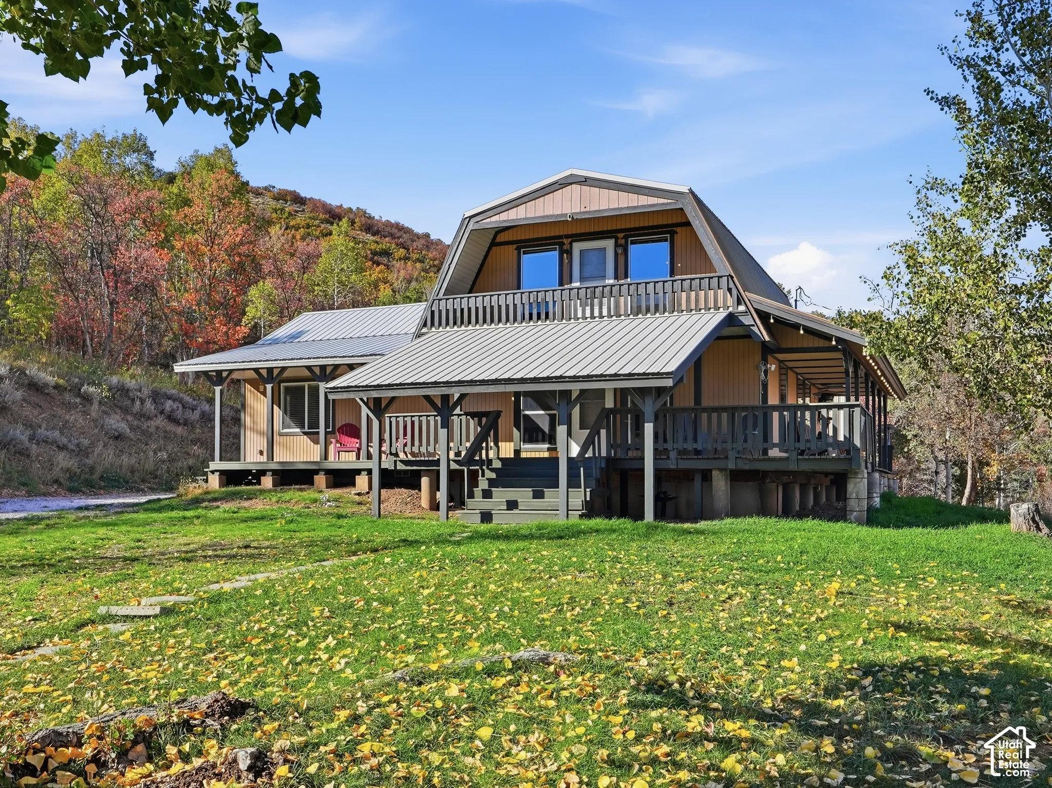 Gambrel-style exterior featuring vertical wood siding, a metal roof, a wraparound porch, and an upper-level railed balcony