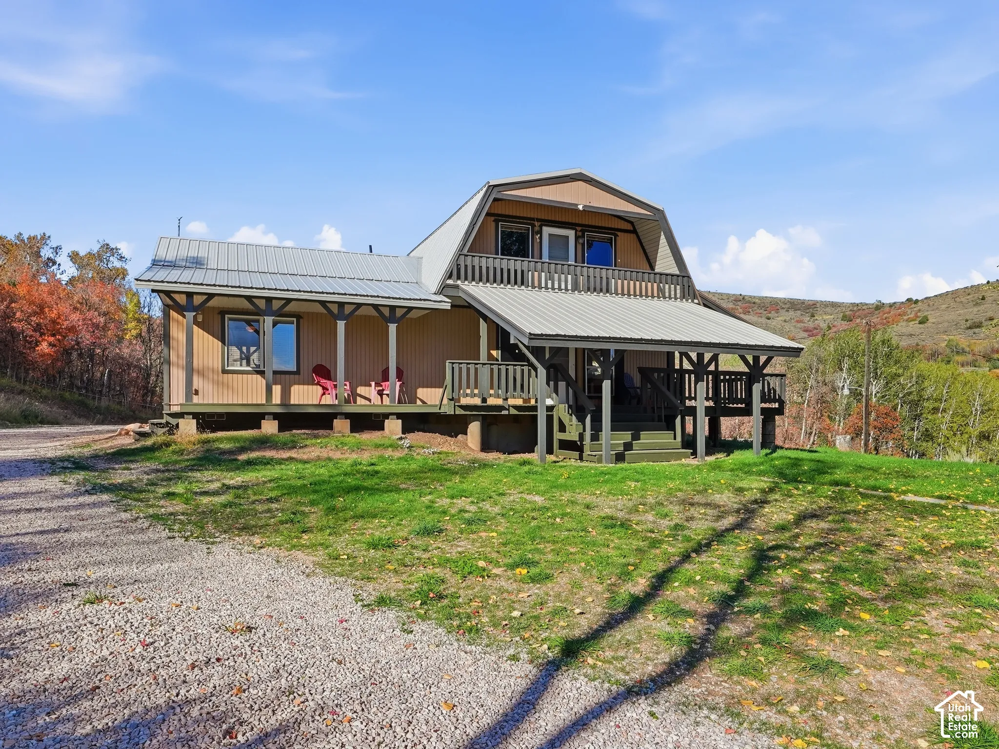 Gambrel-style exterior featuring a metal roof, expansive covered porch, wood-paneled siding, and a second-story deck