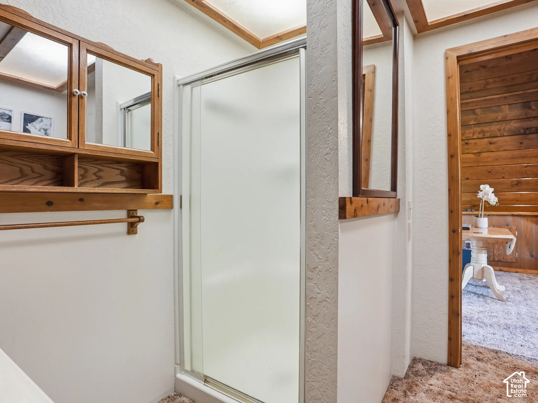 Walk-in shower with frosted glass enclosure, wall-mounted wooden cabinetry with mirrored doors, wood trim detailing, and recessed ceiling lighting